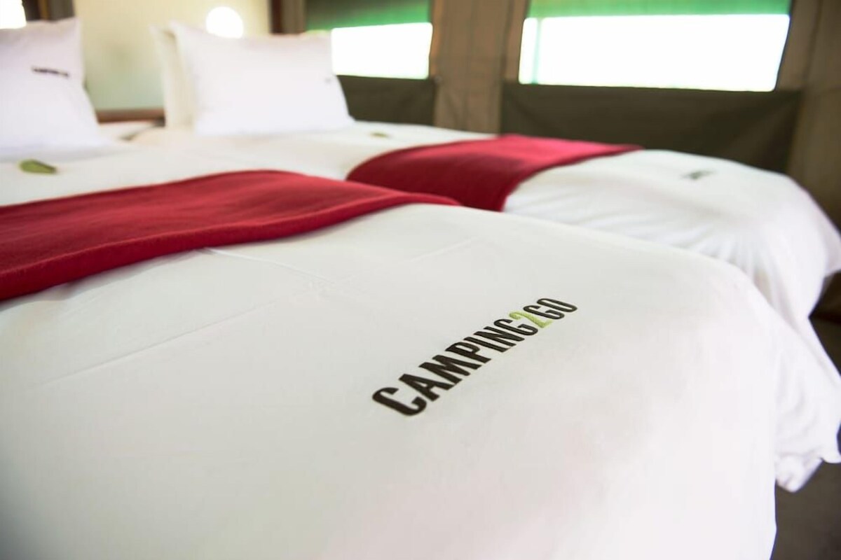 A bed with a white cover and a red blanket, and the word 'CAMPING' visible on the cover.