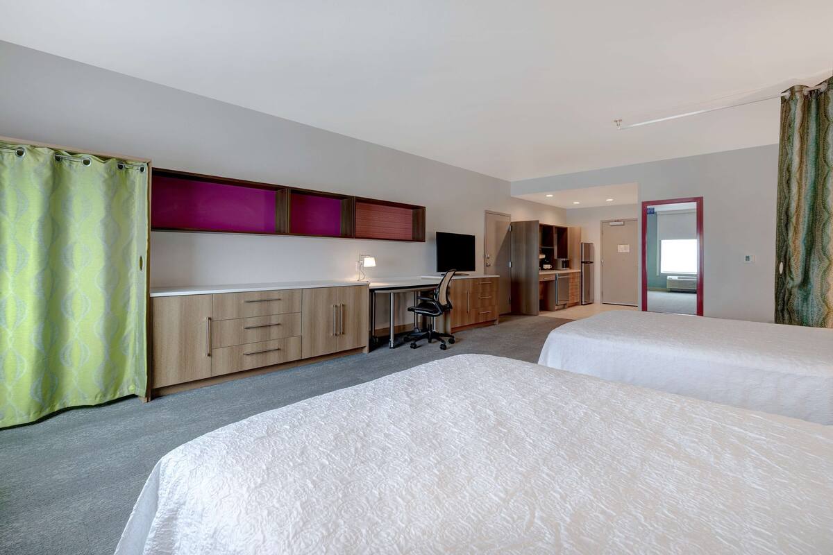Habitación de hotel con dos camas, un escritorio, una silla, un televisor y un armario.