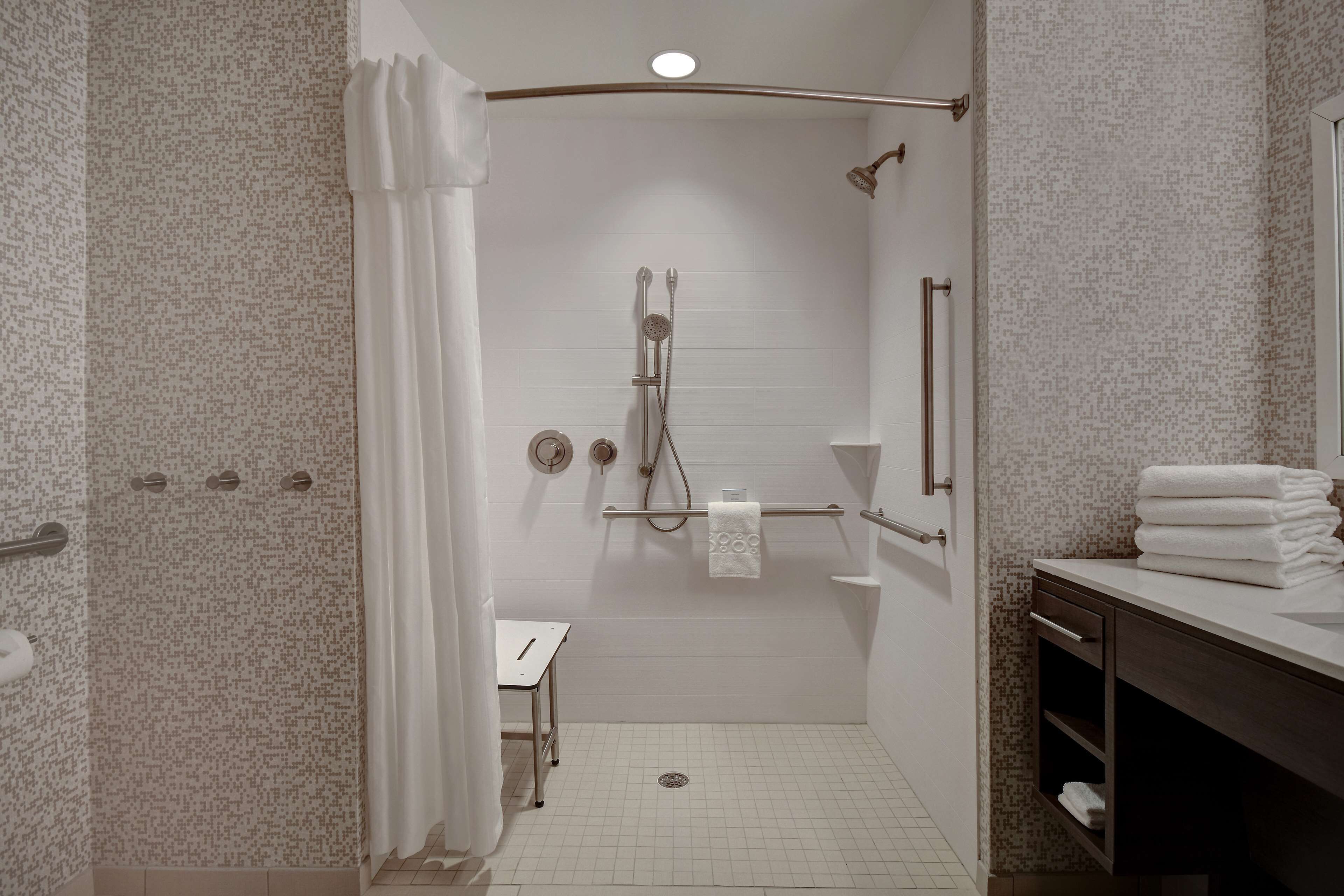 Eine begehbare Dusche mit weißem Duschvorhang, einem Handtuchhalter und einem kleinen Tisch.