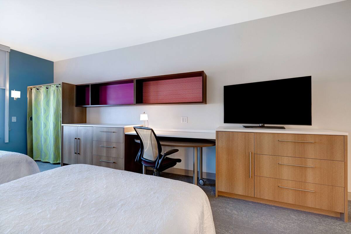 Una habitación de hotel con dos camas, un escritorio con silla, televisión y armario.