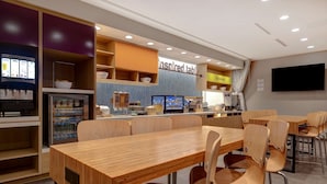 A modern restaurant with wooden tables and chairs, a self-service beverage station, and a TV screen. - Home2 Suites by Hilton Las Vegas Northwest (Las Vegas)