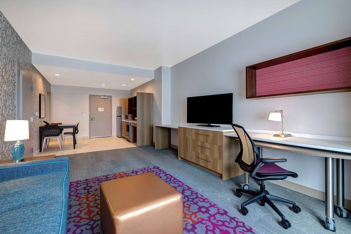 Una habitación de hotel con escritorio, silla, televisor y una pequeña zona de comedor.