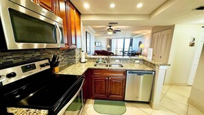 A modern kitchen with stainless steel appliances, wooden cabinets, and a granite countertop. - Beachfront 2BR/2BA condo in Marco Island with pool, WiFi, and coastal views. (Marco Island)