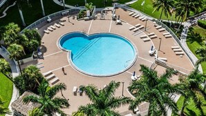 An aerial view of a pool area with a heart-shaped pool, surrounded by lounge chairs and palm trees. - Beachfront 2BR/2BA condo in Marco Island with pool, WiFi, and coastal views. (Marco Island)