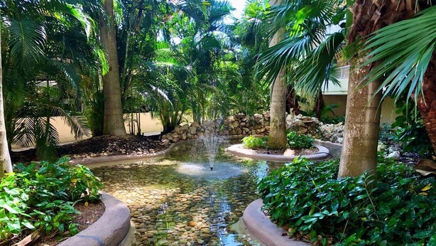 A tranquil garden with a central water feature, surrounded by lush greenery and stone pathways. - Beachfront 2BR/2BA condo in Marco Island with pool, WiFi, and coastal views. (Marco Island)