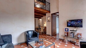 Ein Wohnzimmer mit Glastisch, zwei Sofas, einem an der Wand befestigten Fernseher und einer Treppe, die zu einer oberen Etage führt.