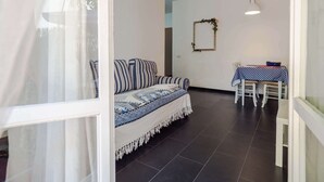A room with a sofa, a table with a checkered tablecloth, a mirror on the wall, and a hanging light fixture. - Sciacchetrà Apartment with AC (Monterosso al Mare)