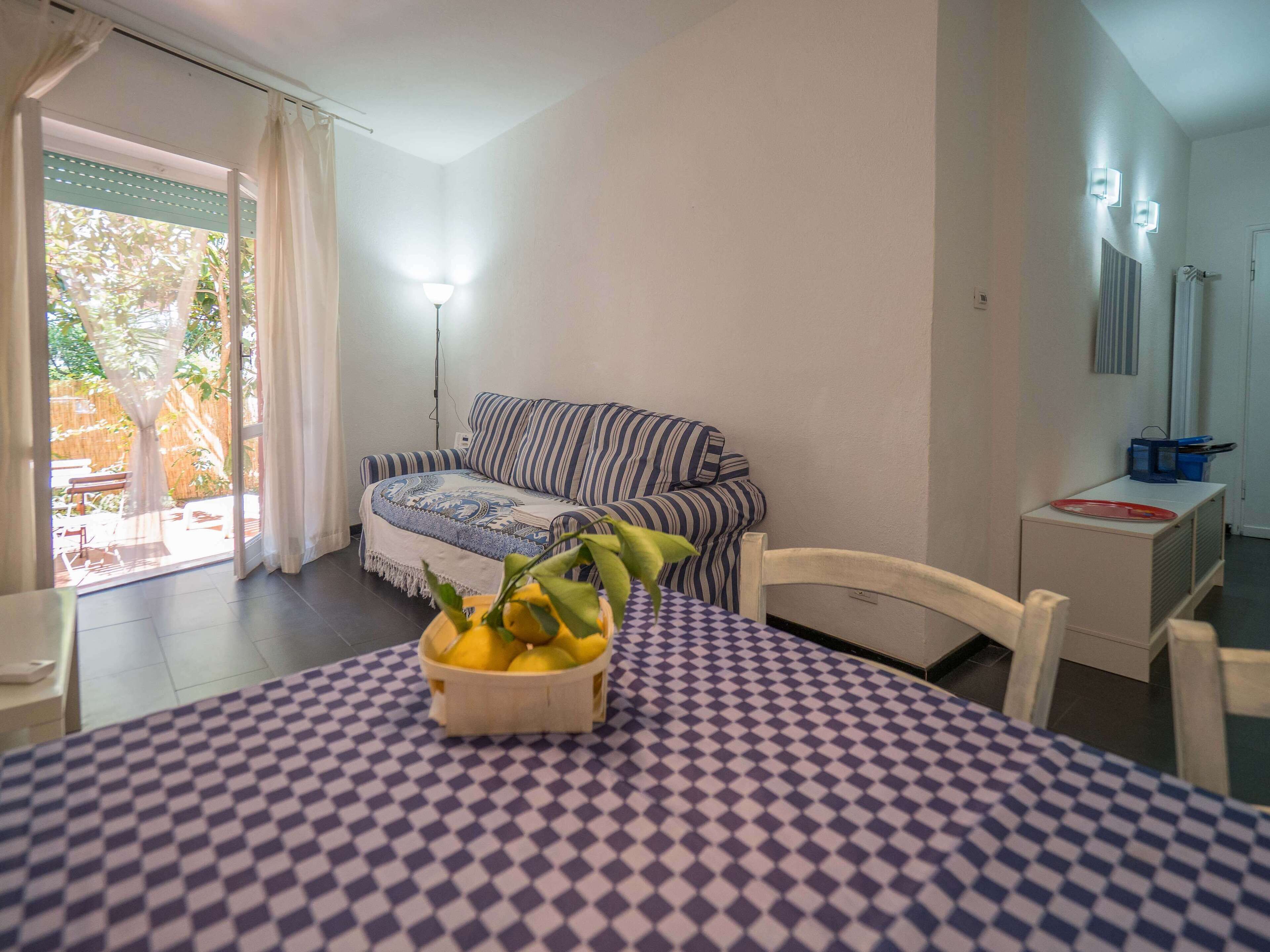 Una habitación con mantel a cuadros, sofá a rayas, una mesita con frutero y vistas a un jardín por una puerta corrediza.