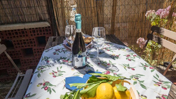 A table set with a bottle of wine, glasses, and a bowl of lemons on a tablecloth with a fruit pattern. - Sciacchetrà Apartment with AC (Monterosso al Mare)