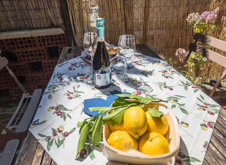 A table set with a bottle of wine, glasses, and a bowl of lemons on a tablecloth with a fruit pattern.