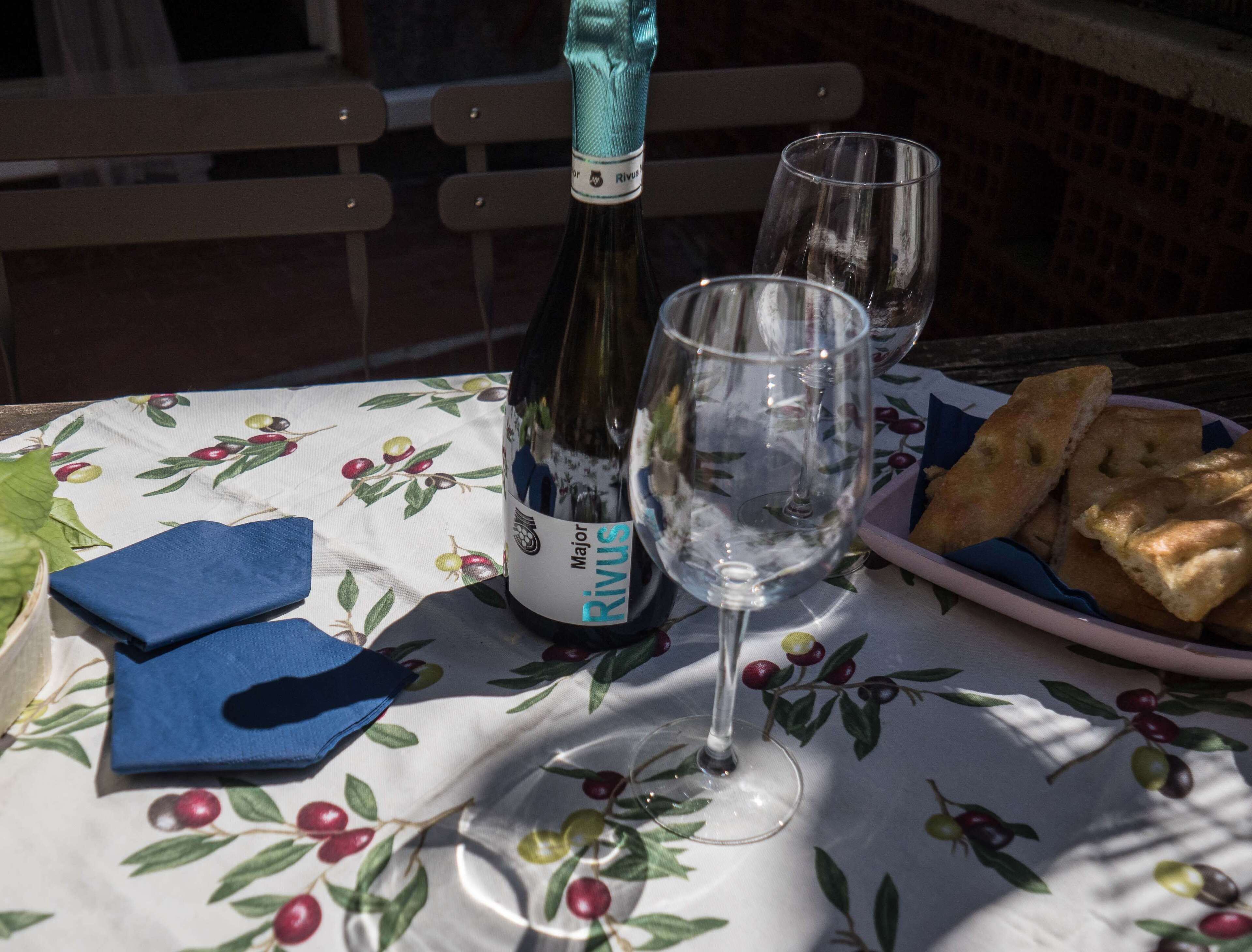Una botella de vino, una copa de vino y un plato de pan sobre una mesa con mantel floreado.