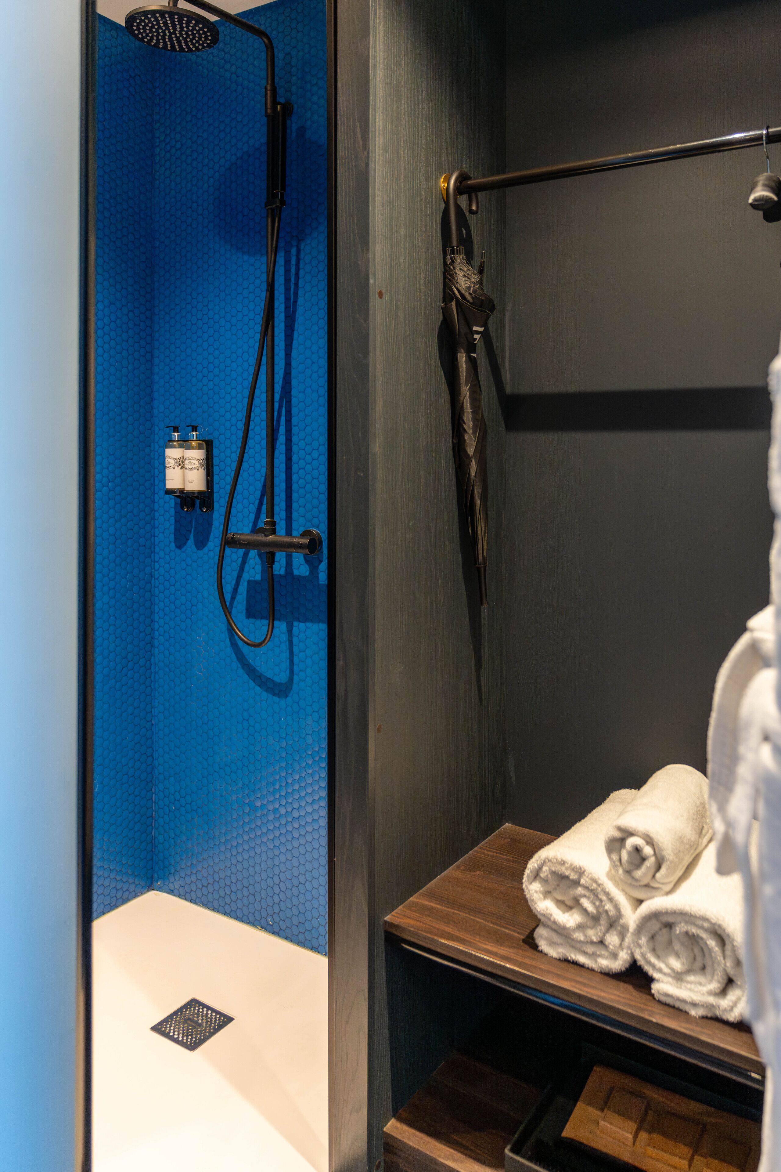 A bathroom with a blue shower enclosure, a towel rack with towels, and a wooden shelf.