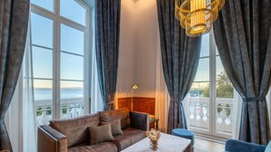 A spacious living room with a large window, a sofa, a coffee table, and a chandelier. - The Editory Riverside Hotel, an Historic Hotel (Lisbon)