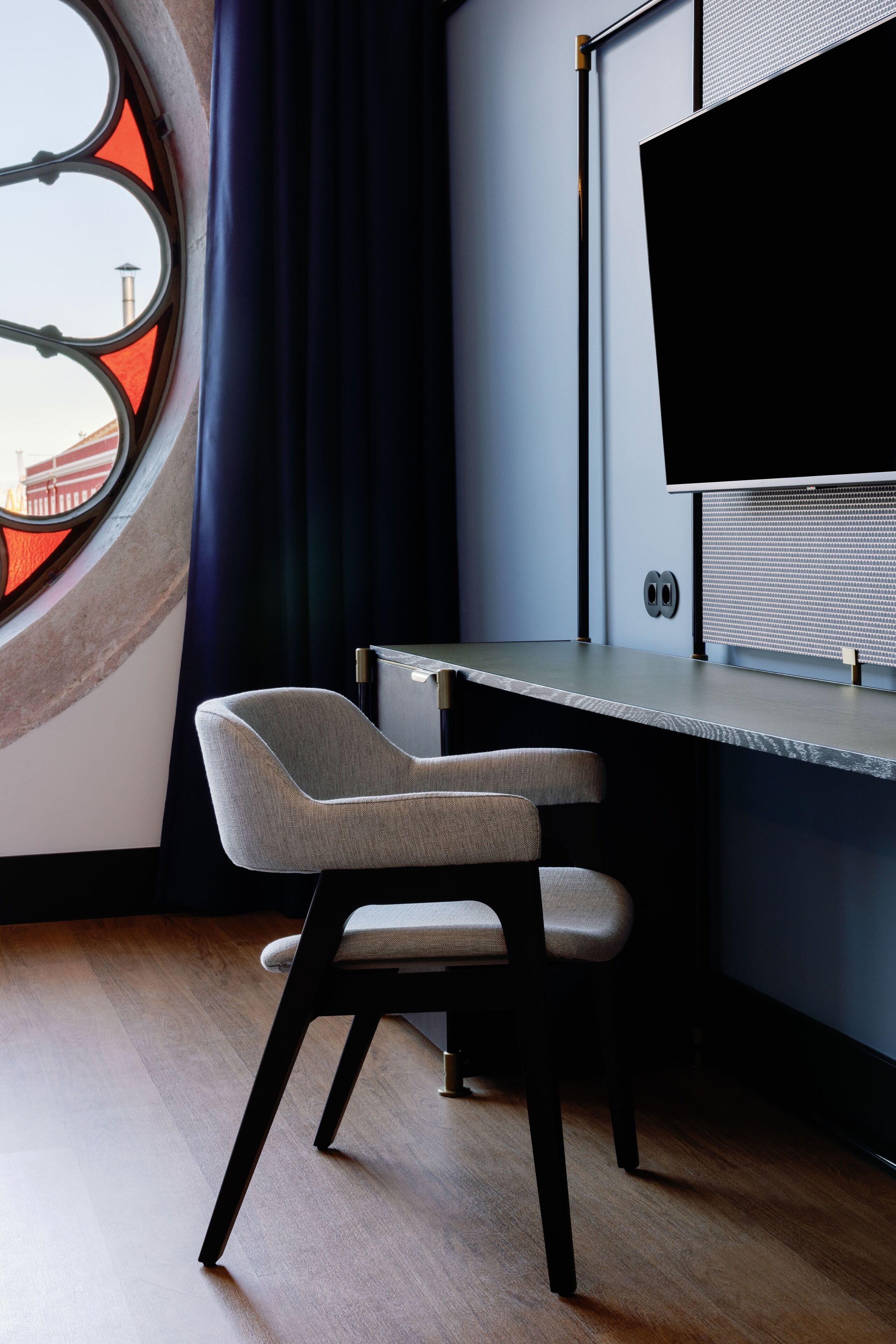 A modern office space with a desk, two chairs, a large window with a view of a bridge, and a flat-screen TV mounted on the wall.