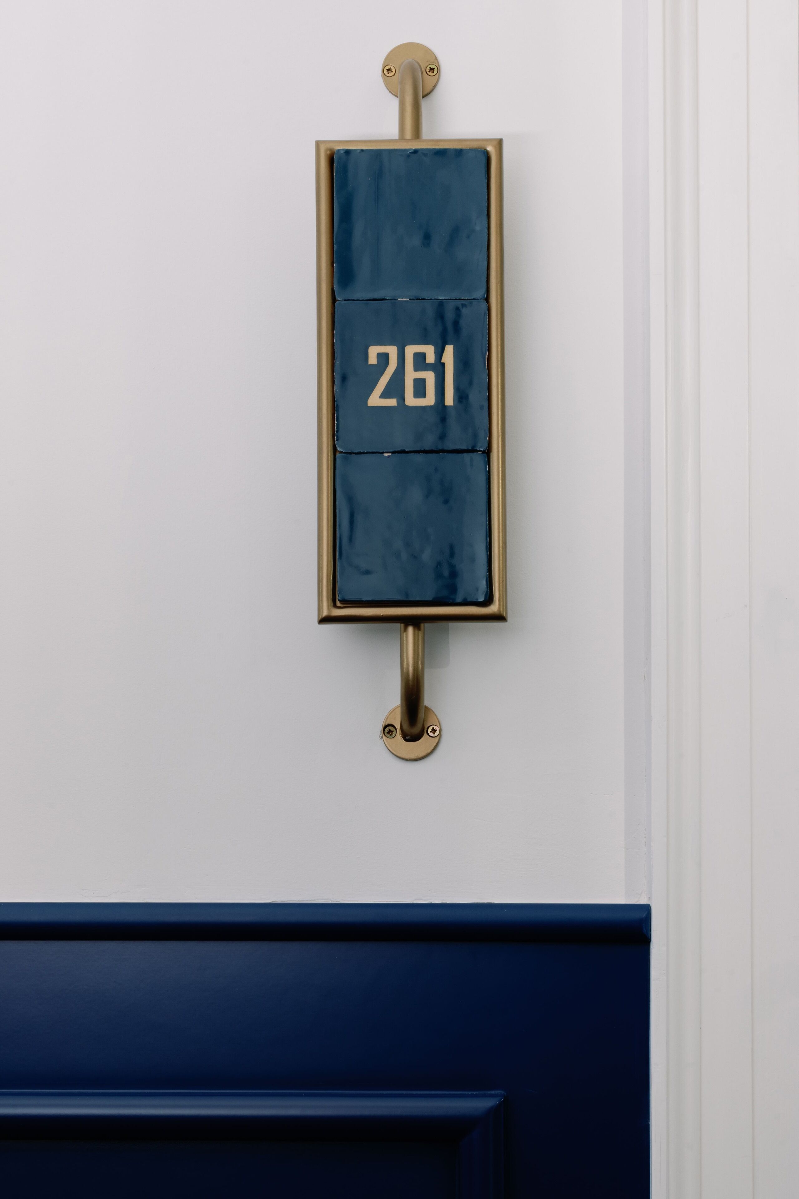 En blå och guldfärgad brevlåda med nummer 261, placerad på en vit vägg.