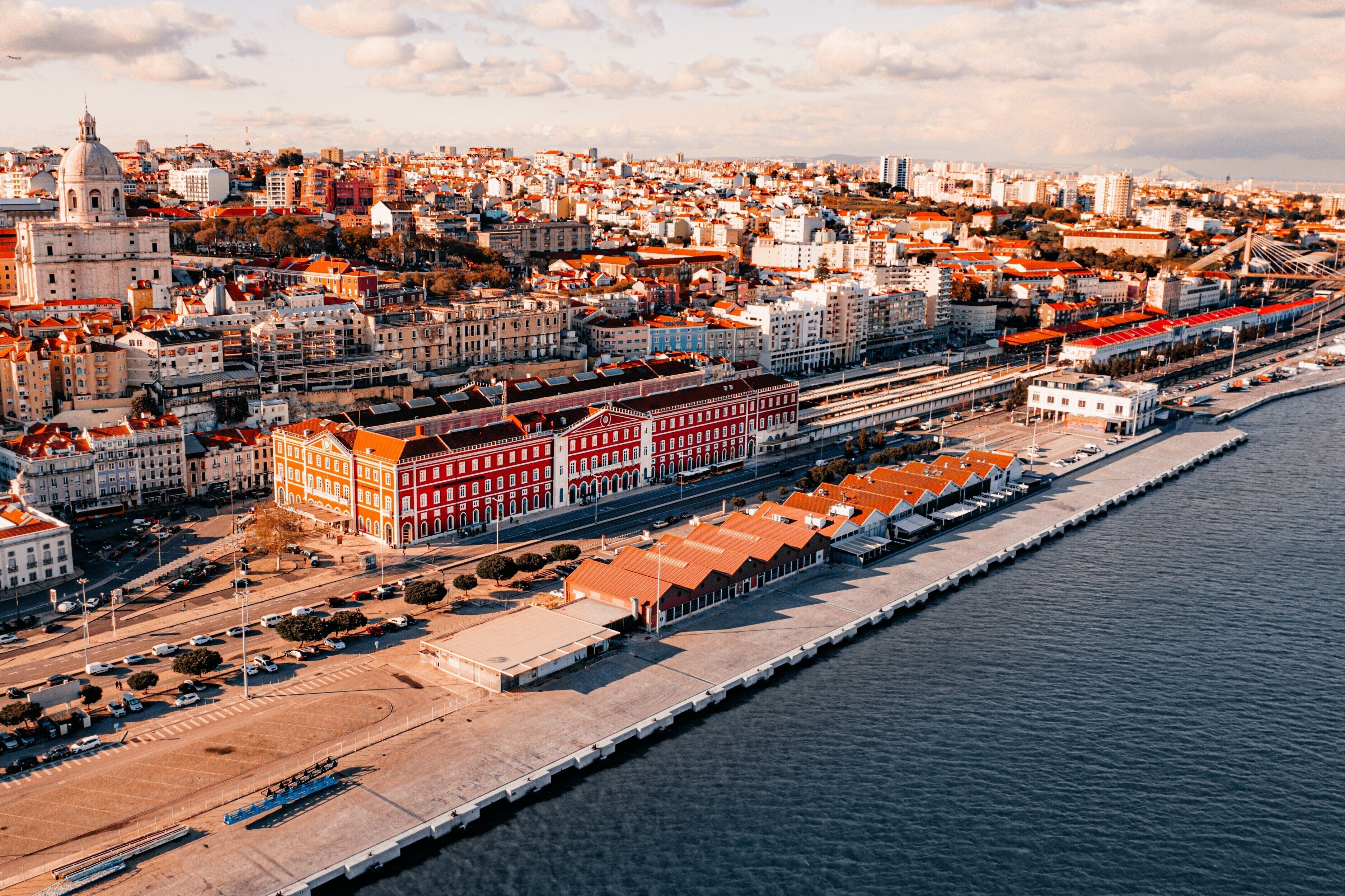 An aerial view of a city with a prominent waterfront, including a long pier and a large red building with a white facade.