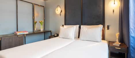 A modern hotel room with a large bed, bedside tables, a mirror, and wall-mounted lights.