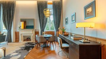 A room with a fireplace, dining table, chairs, a desk with a lamp, and a large mirror.