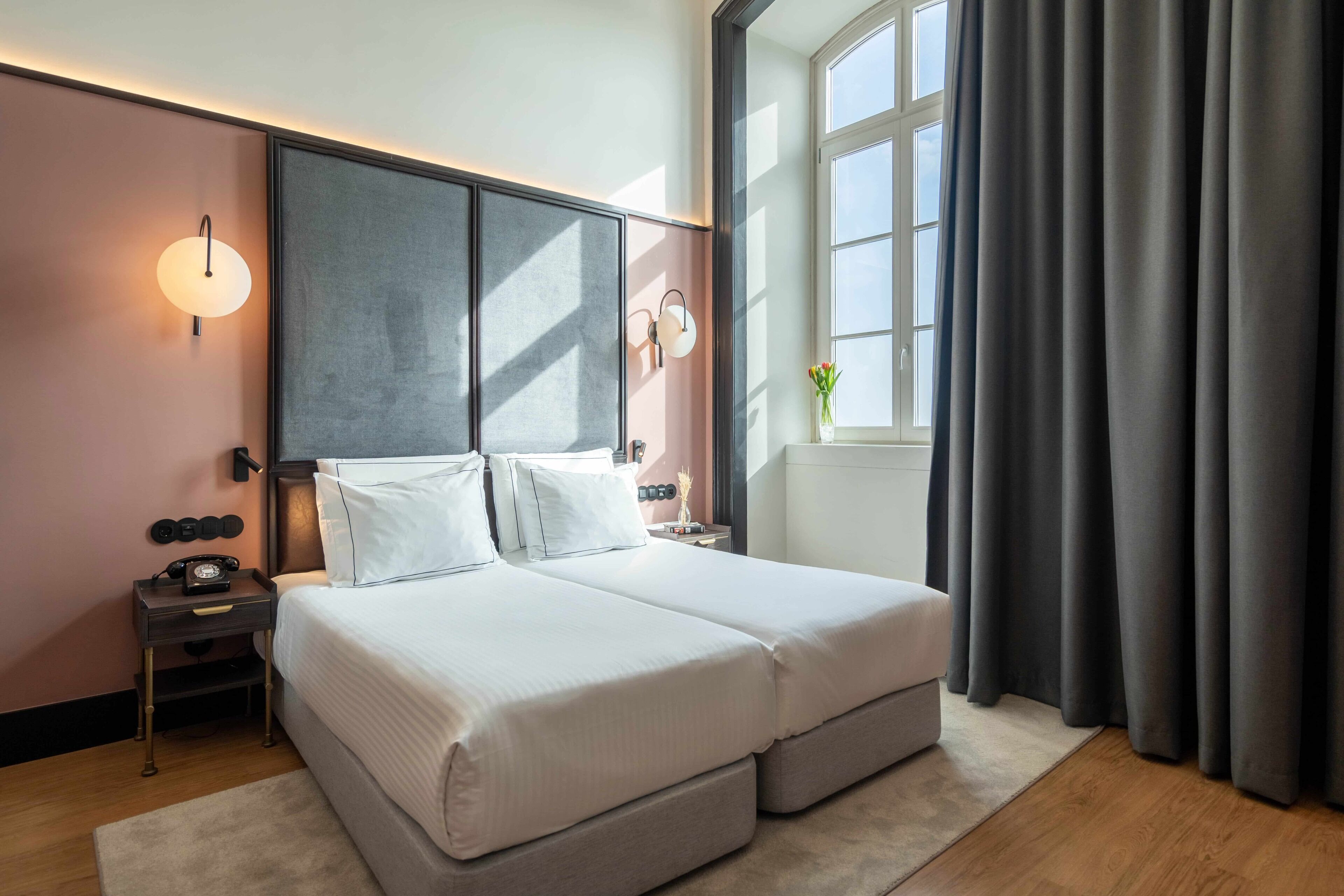 A modern bedroom with a large bed, bedside lamps, a nightstand, and a window with curtains.