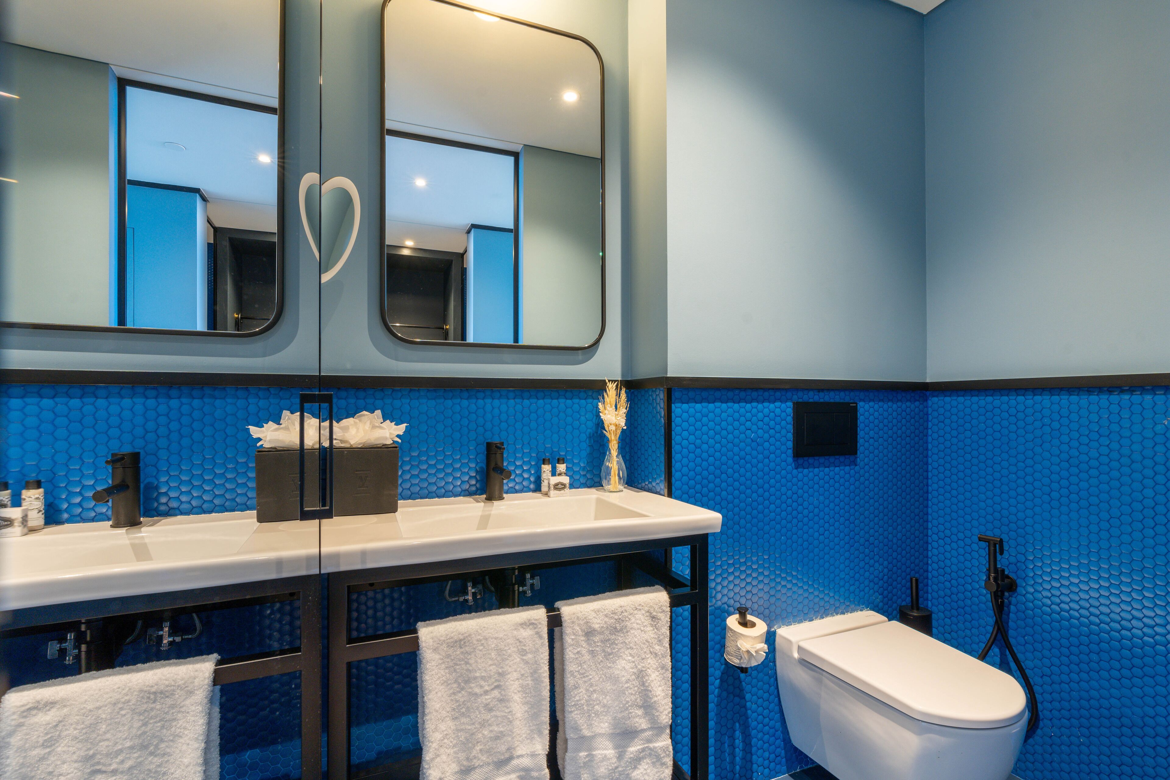 A bathroom with a blue tiled wall, a white sink, a mirror, and a toilet.
