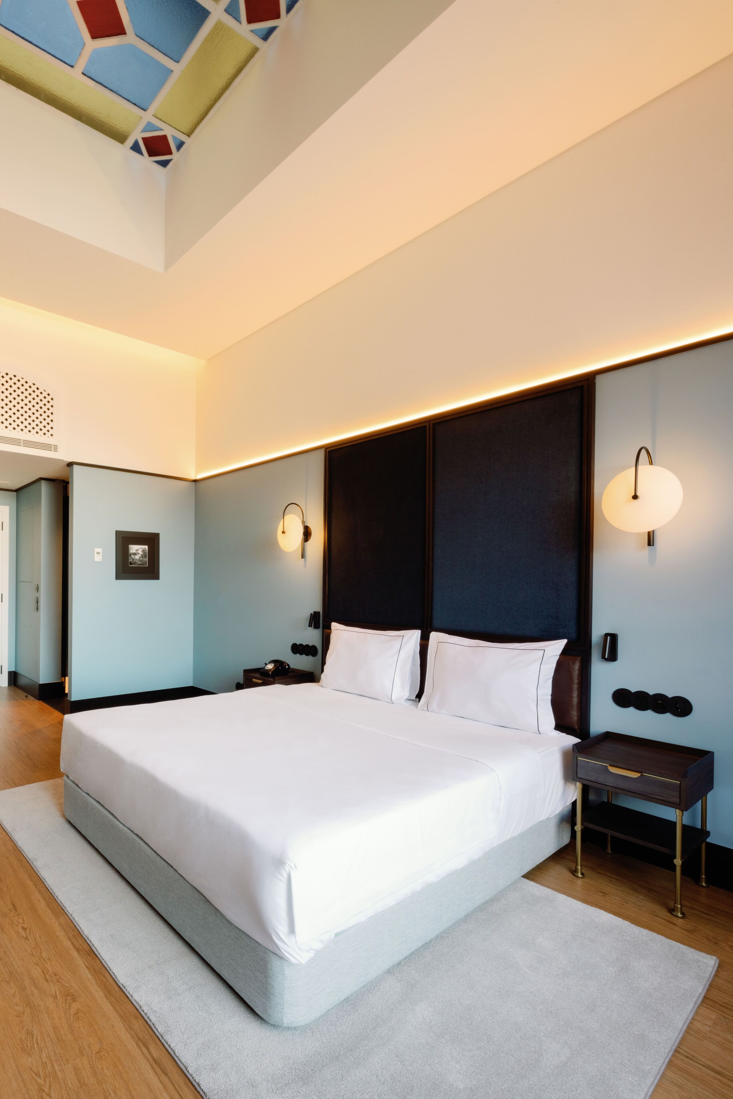 Una habitación de hotel moderna con una cama grande, mesitas de noche y un techo con diseño geométrico.