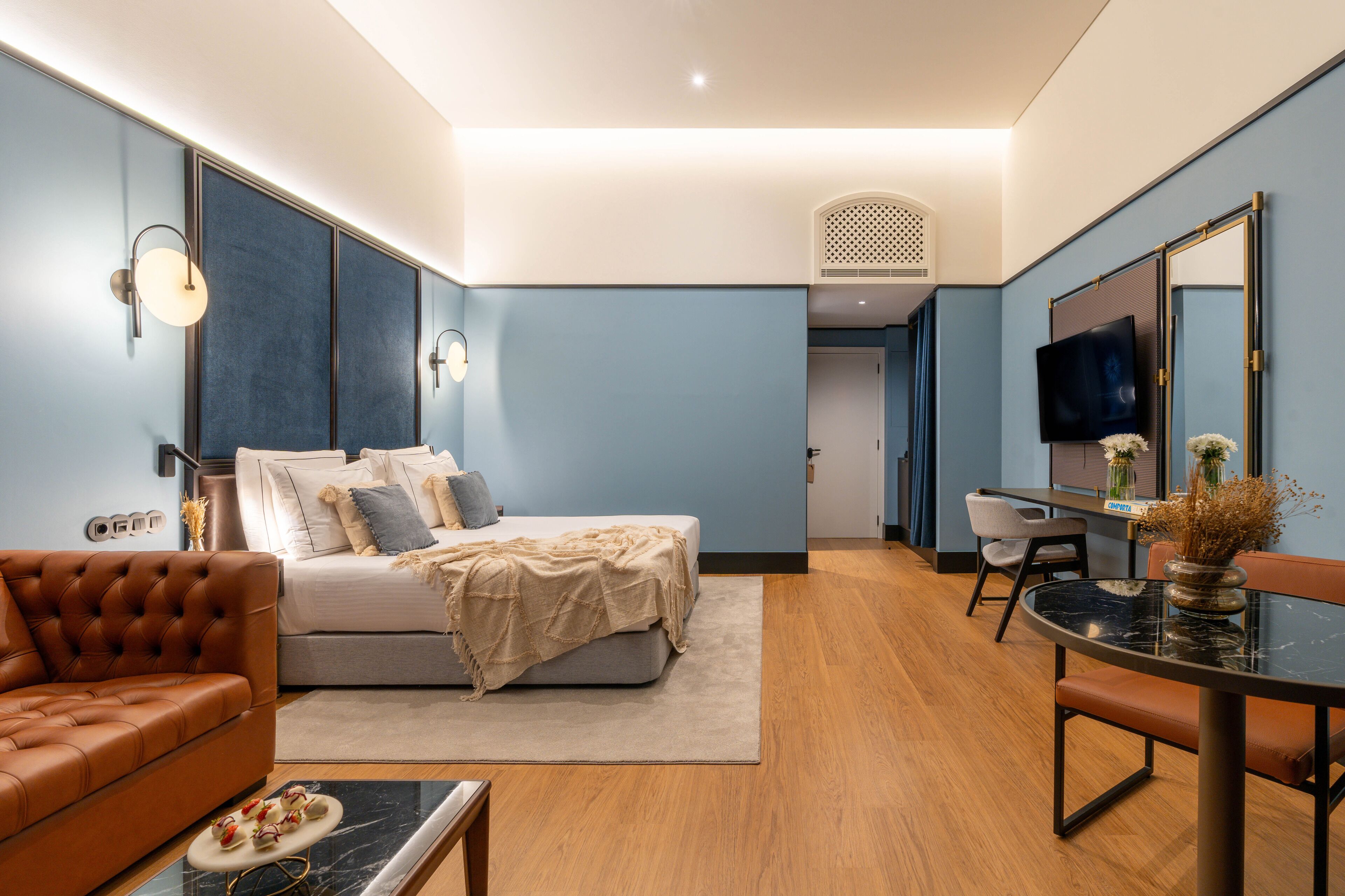 Una habitación de hotel moderna con cama, sofá, mesa de comedor y televisor.