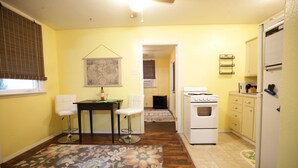 A compact kitchen with a refrigerator, stove, and a dining area with two chairs and a table. - Bee Our Guest | East Pensacola Heights Rental Near Downtown Pensacola Beach (Pensacola)
