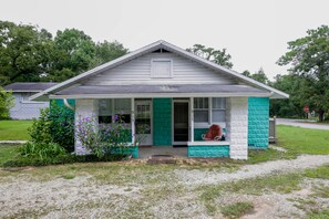 A single-story house with a porch, a small front yard, and a stop sign in the background.