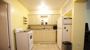 A compact kitchen with white appliances, a sink, and a trash can. - Bee Our Guest | East Pensacola Heights Rental Near Downtown Pensacola Beach (Pensacola)