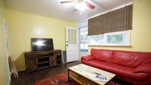 A living room with a red leather couch, a wooden coffee table, a television on a wooden cabinet, and a patterned rug. - Bee Our Guest | East Pensacola Heights Rental Near Downtown Pensacola Beach (Pensacola)