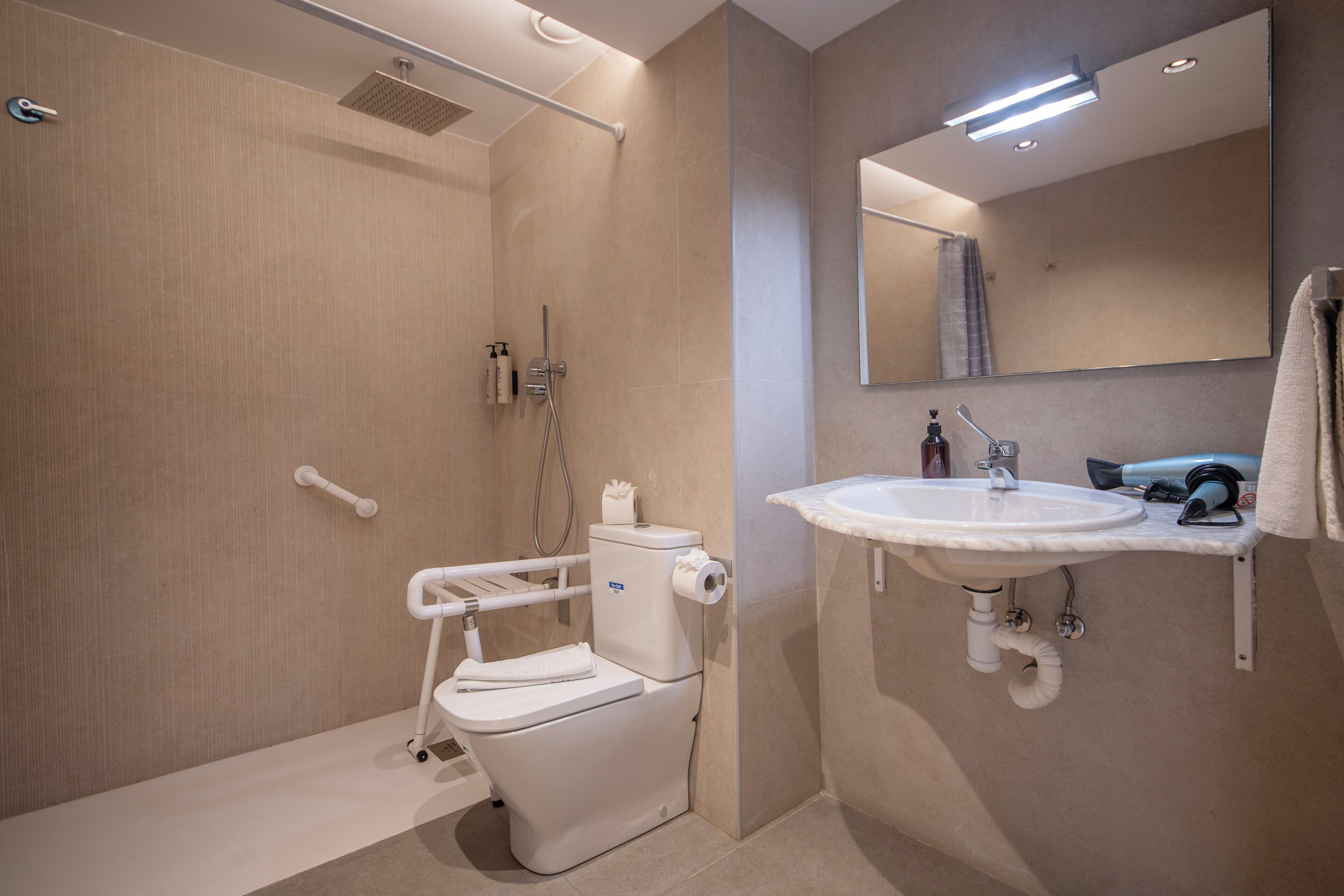A modern bathroom with a walk-in shower, a toilet with a grab bar, a sink with a mirror, and a towel rack.
