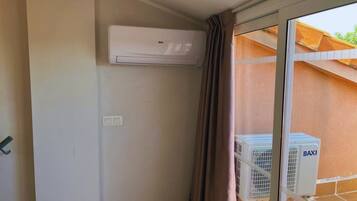 Una habitación con puerta de vidrio corredera, aire acondicionado de pared y ventana con vista a un edificio.
