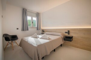Un dormitorio moderno con una cama, mesitas de noche, una silla y un ventanal con cortinas.