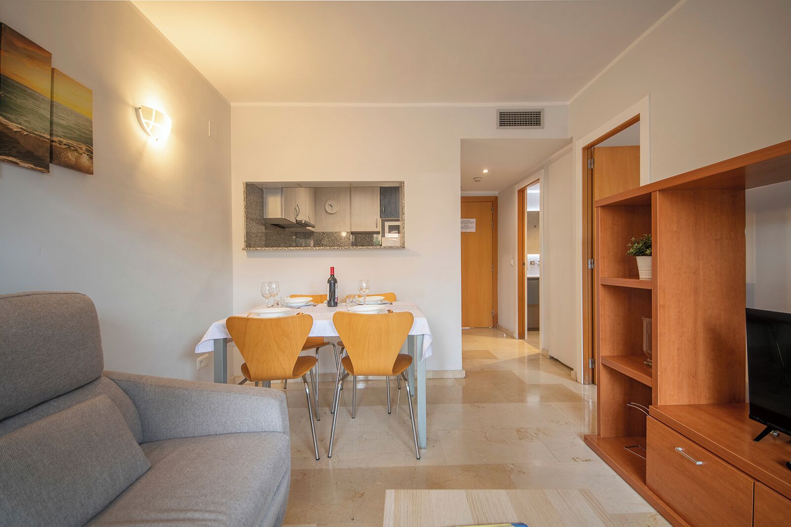 A modern living room with a grey sofa, a dining table with chairs, a wooden TV stand, and a kitchen area in the background.