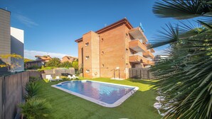 A residential building with a swimming pool, green lawn, and a wooden fence. - Marsol Apartamentos Turisticos (Castelldefels)