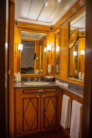 Un baño con tocador de madera, un espejo grande y un lavamanos. Hay toallas colgadas en la pared y un dispensador de jabón.