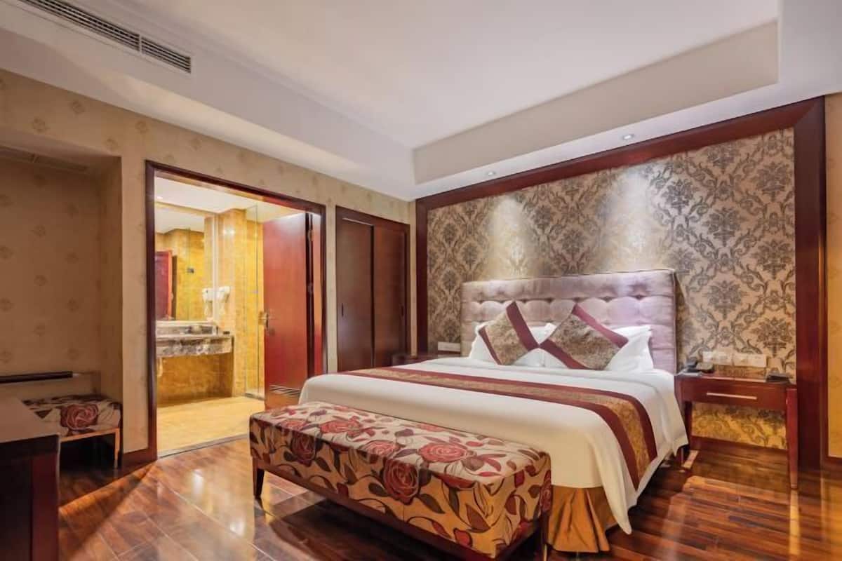 Une chambre d’hôtel avec un grand lit, une banquette, une table de chevet et une salle de bain visible à travers une porte ouverte.