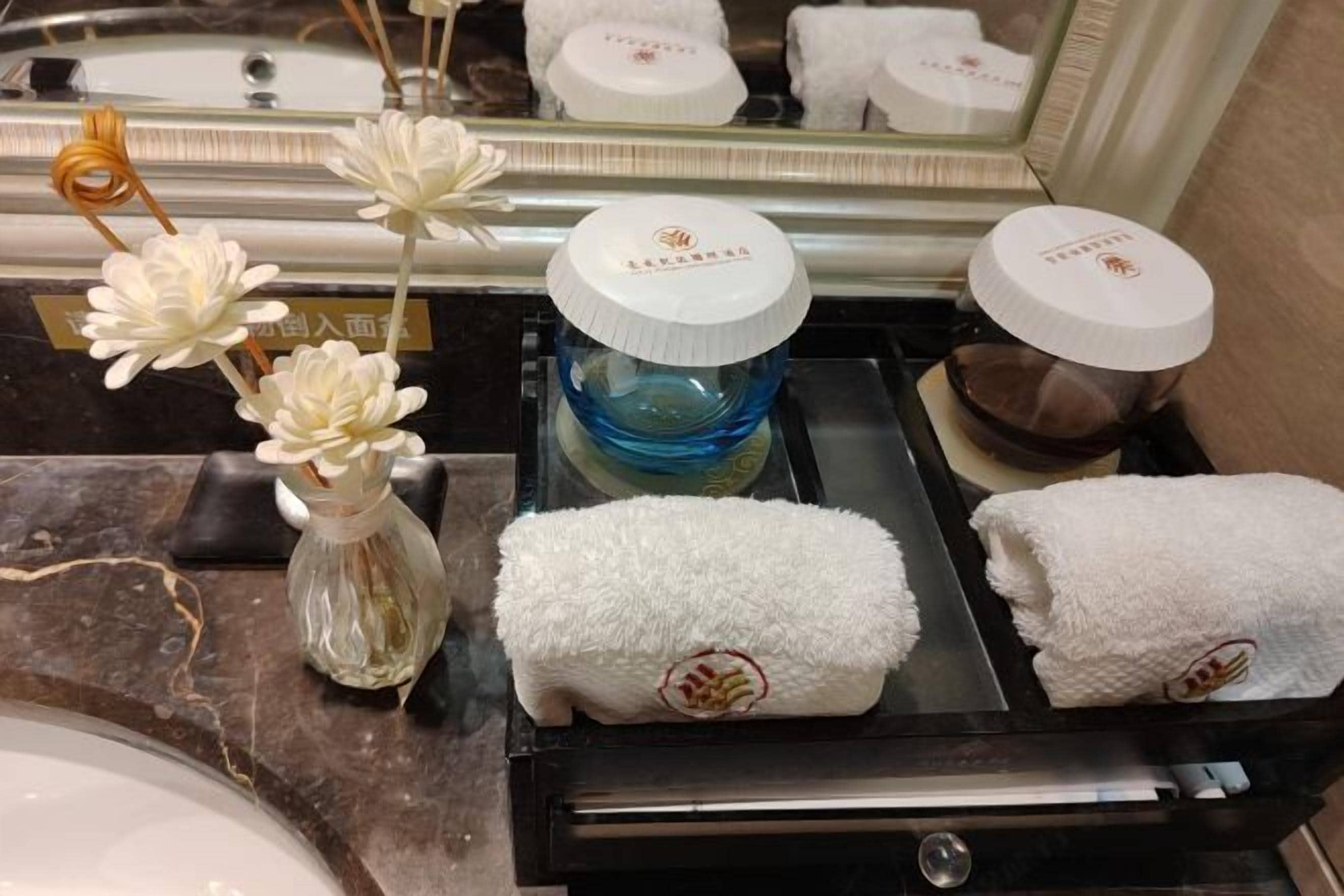 Un tocador de baño con espejo, un perchero y un pequeño jarrón con flores blancas.