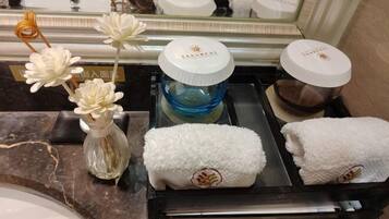 Un tocador de baño con espejo, un perchero y un pequeño jarrón con flores blancas.