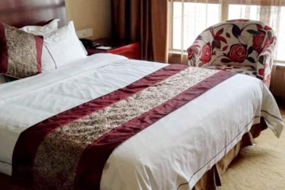 Une chambre d’hôtel avec un lit, un fauteuil à motifs floraux et une fenêtre avec des rideaux.