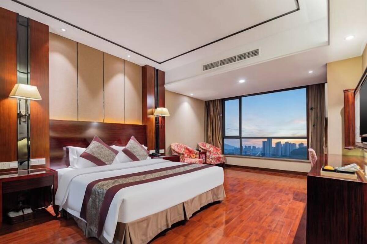 Une chambre d’hôtel avec un grand lit, deux lampes de chevet, une télévision et une vue sur le panorama de la ville.