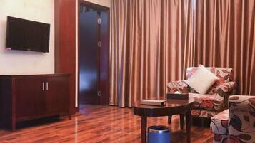 Habitación de hotel con piso de madera, televisor montado en la pared, sofá con tapicería floral, una mesita y un bote de basura azul.