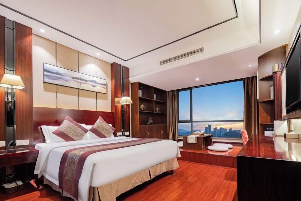 Une chambre d’hôtel moderne dotée d’un grand lit, d’un bureau, d’une télévision et offrant une vue sur le panorama urbain.