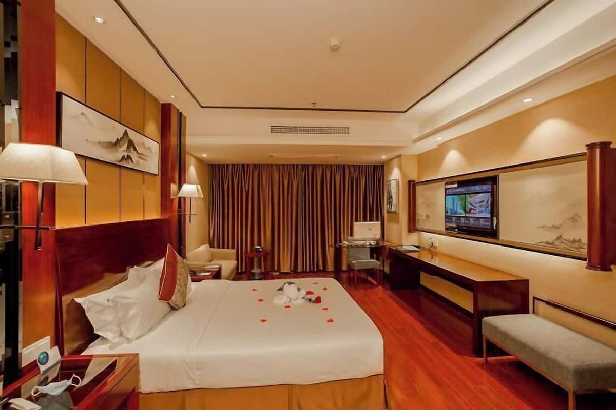 Une chambre d’hôtel comprenant un lit, des tables de chevet, un bureau, une chaise, un téléviseur et une grande fenêtre avec des rideaux.