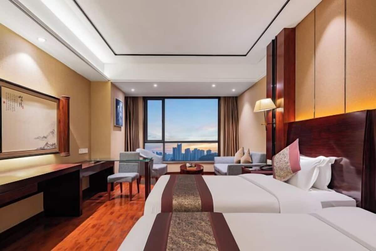 Une chambre d’hôtel avec un grand lit, un bureau, une chaise, un canapé et une vue sur le panorama urbain.