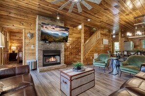 A cozy cabin interior with a fireplace, comfortable seating, and a staircase leading to the upper level.