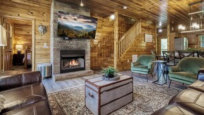 A cozy cabin interior with a fireplace, leather sofas, a dining area, and a staircase leading to the upper level. - Cozy Bear Lodge-peaceful, easy access, beautiful view (Sevierville)