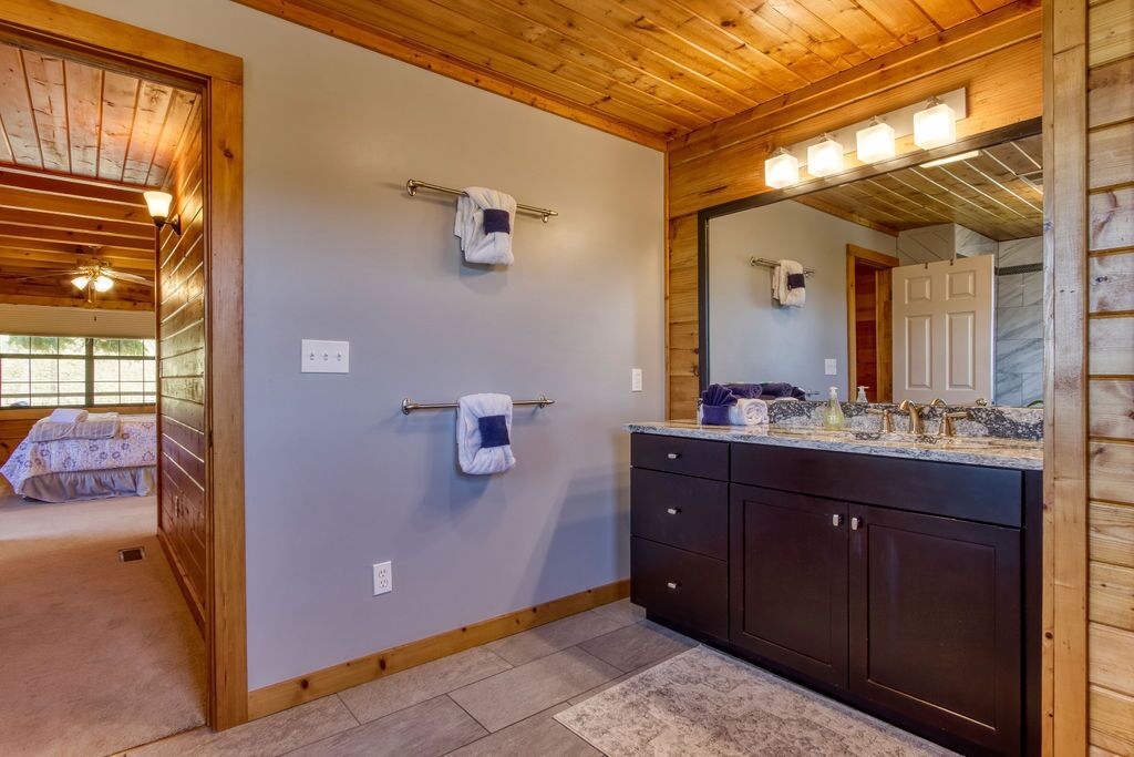 A bathroom with wooden ceiling beams, a large mirror, dark cabinets, and two towels on towel bars.