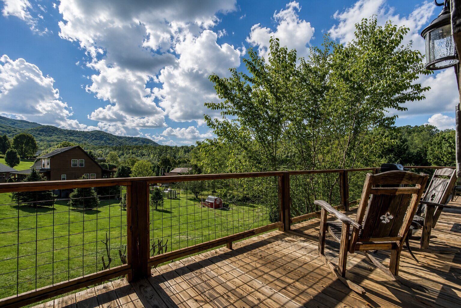 A wooden deck with a view of a green field, a tree, and a house in the background.