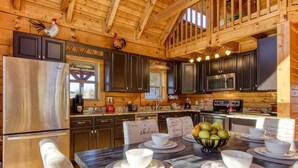 A wooden cabin kitchen with dark cabinets, a stainless steel refrigerator, and a dining table set with white bowls and plates. - Picture Perfect , Panoramic Mountain Views, $560 FREE tickets each paid day! (Sevierville)